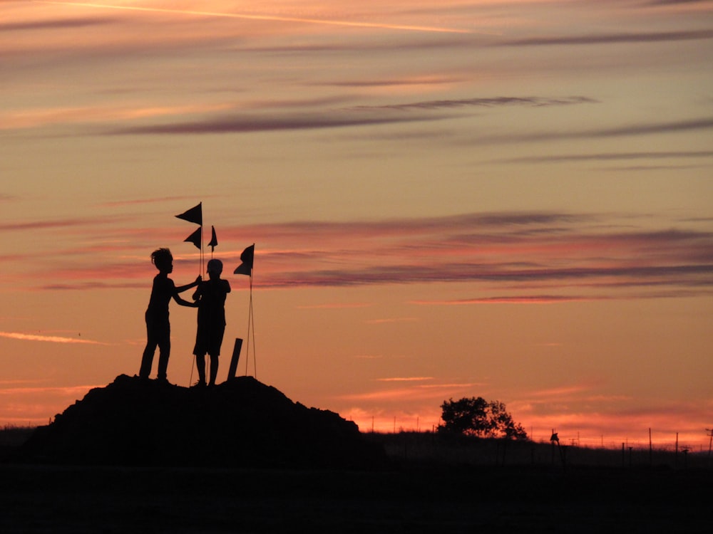 silhouette di 2 persone in piedi sulla roccia durante il tramonto