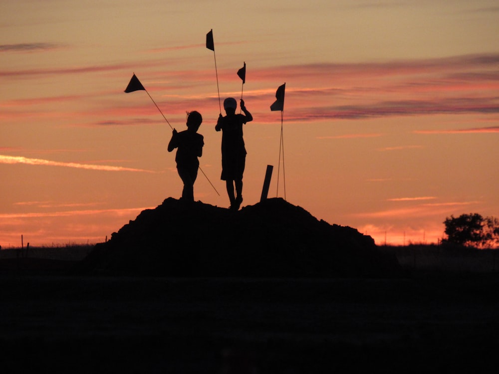 silhouette of 2 person holding flags during sunset