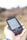 A hand holds a portable GPS device displaying a map. The device shows navigation buttons and the brand name 'TwoNav'. The background is blurred, suggesting outdoor surroundings.