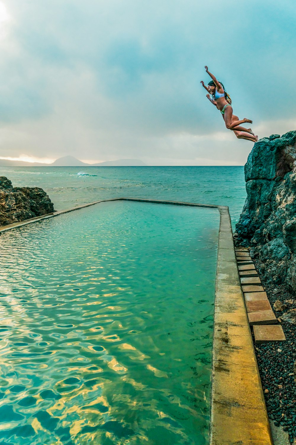 woman jumping from a dock to a body of water