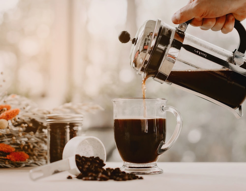 person pouring coffee on clear glass mug