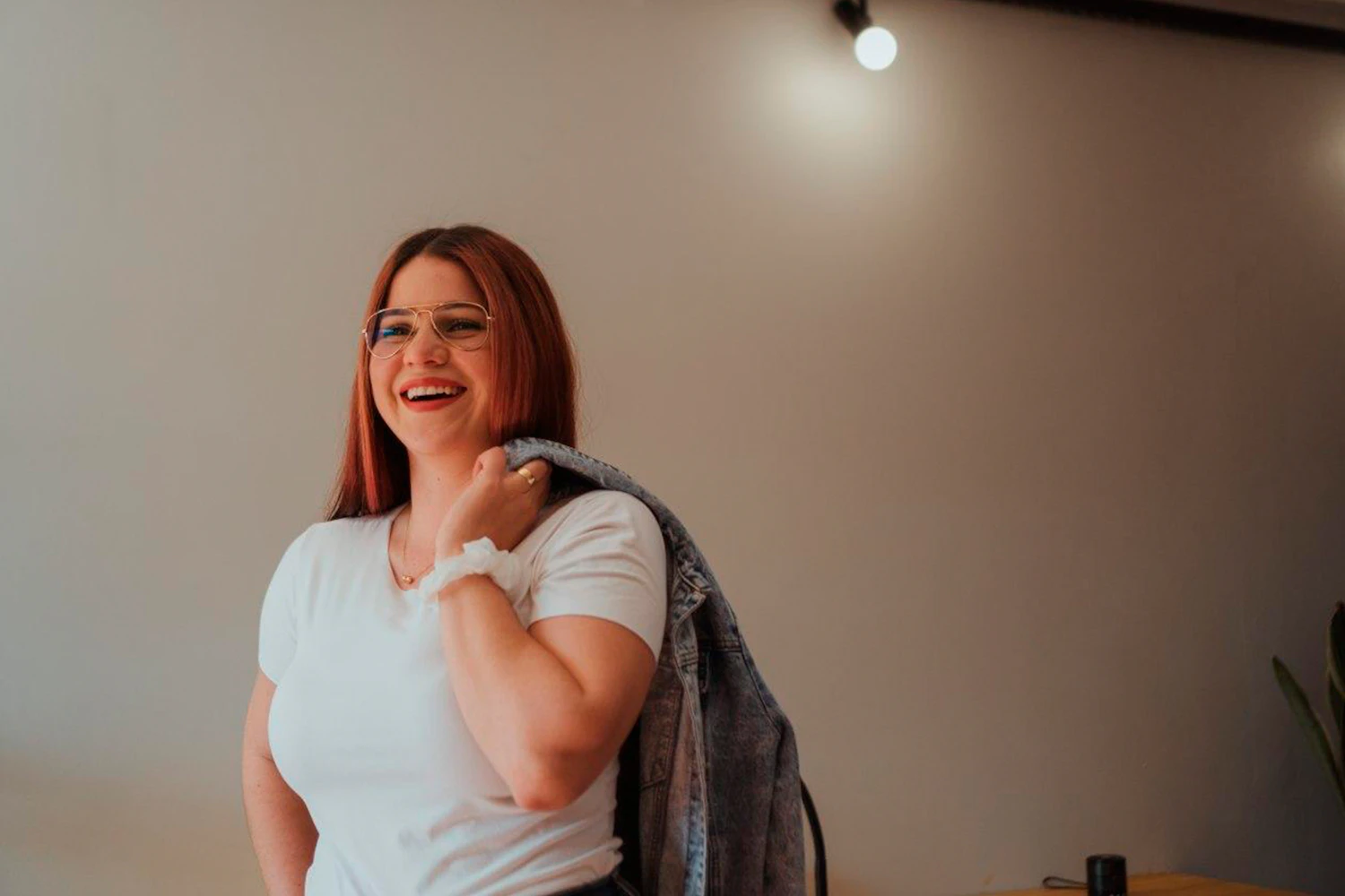 A red-haired facialist in a white t-shirt laughing in a warm, plain room