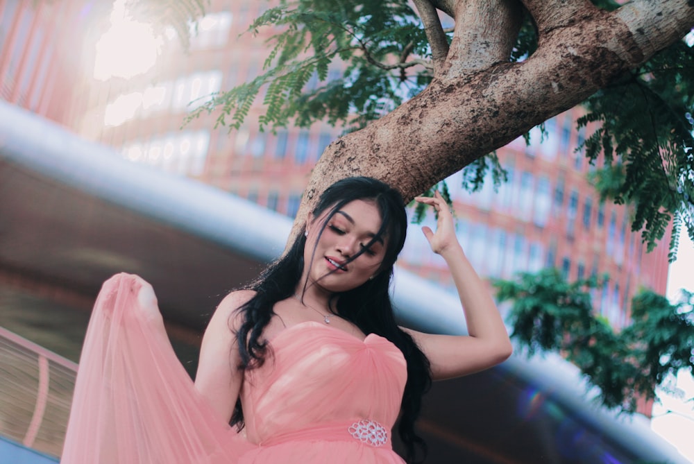 woman in pink sleeveless dress leaning on brown tree