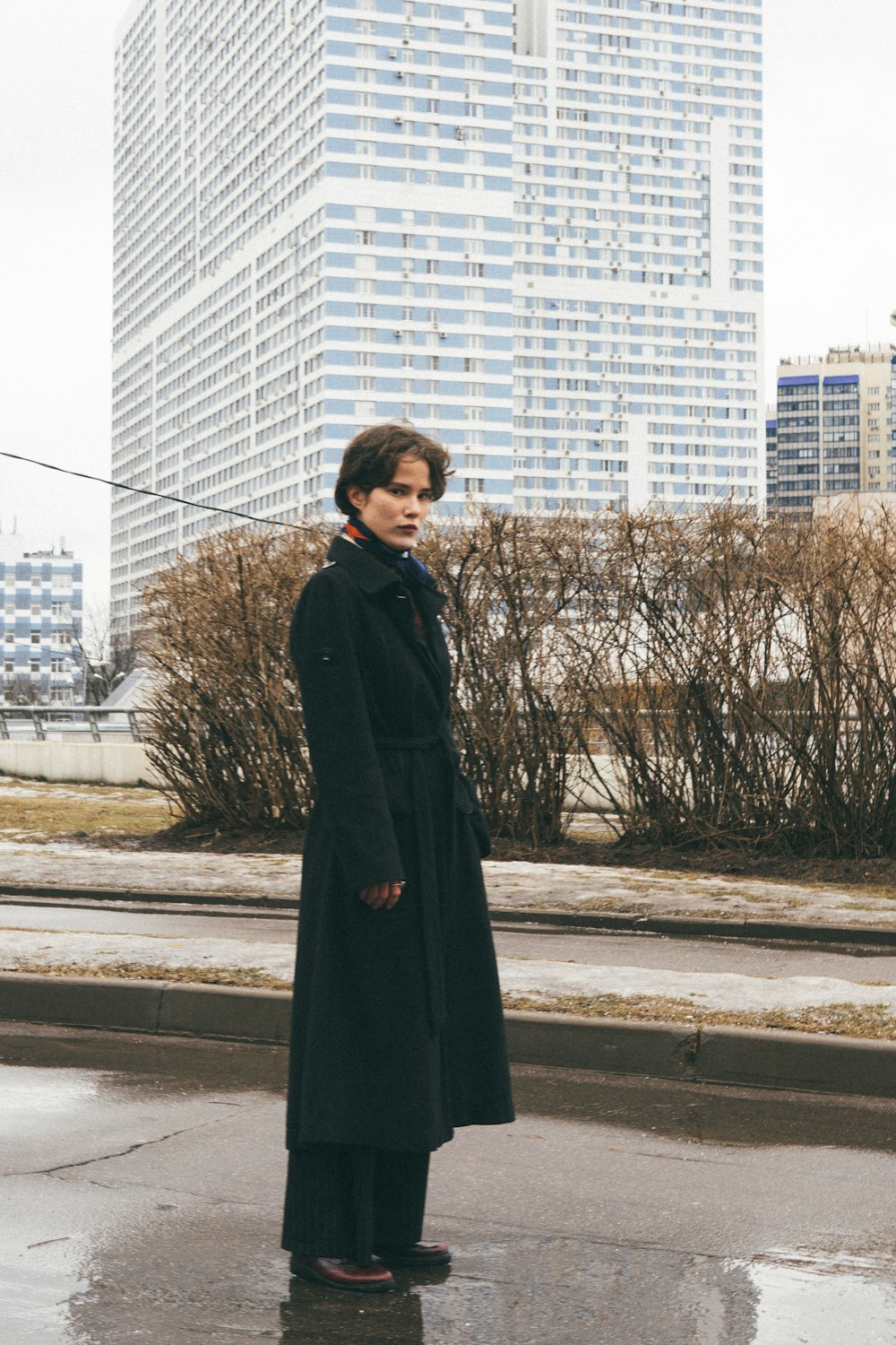 woman in black coat standing on sidewalk during daytime