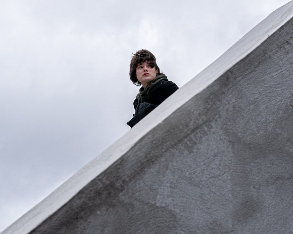 man in black jacket leaning on gray concrete wall