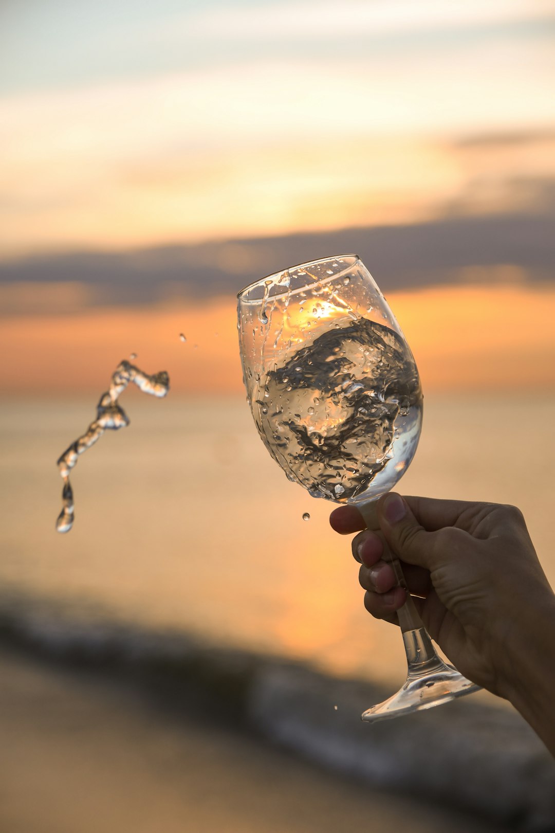 person holding clear wine glass with water during sunset