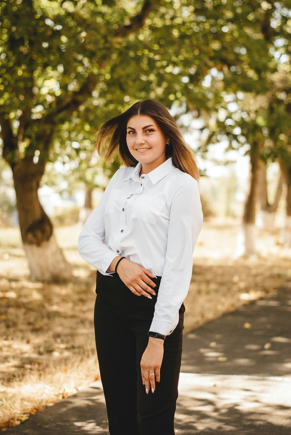 woman in white dress shirt and black pants standing near green trees during daytime