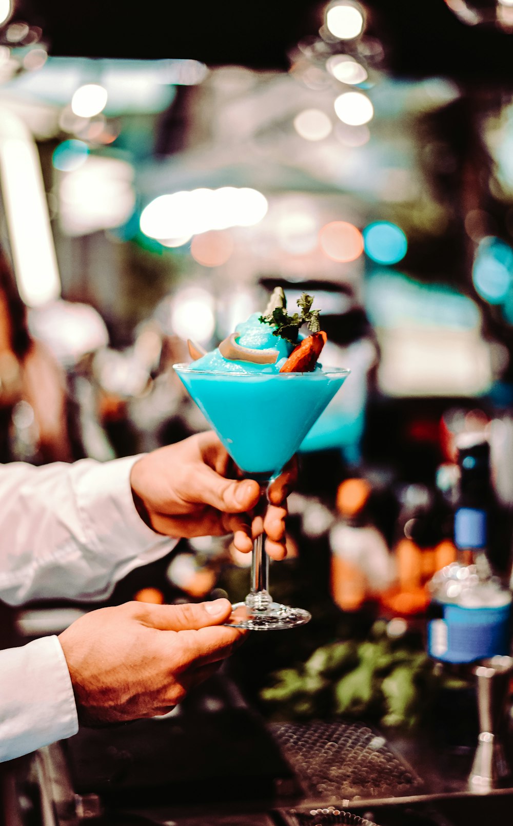 person holding clear cocktail glass with pink liquid