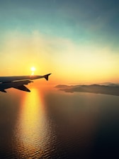 A sleek airplane soaring above a golden sunset over the Himalayas.