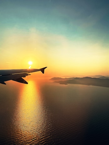 A sleek airplane soaring above a golden sunset over the Himalayas.