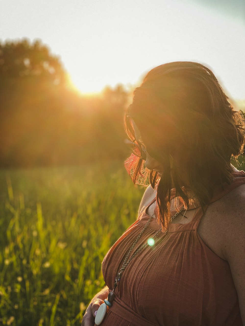 Frau in braunem ärmellosem Kleid steht bei Sonnenuntergang auf grünem Rasen