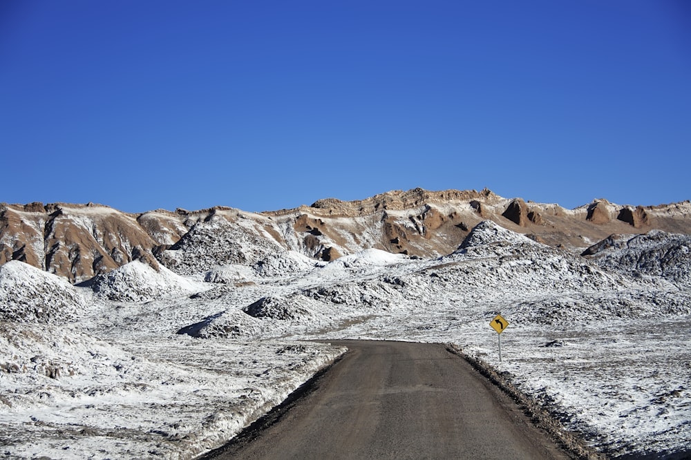 Carretera gris entre montañas cubiertas de nieve durante el día