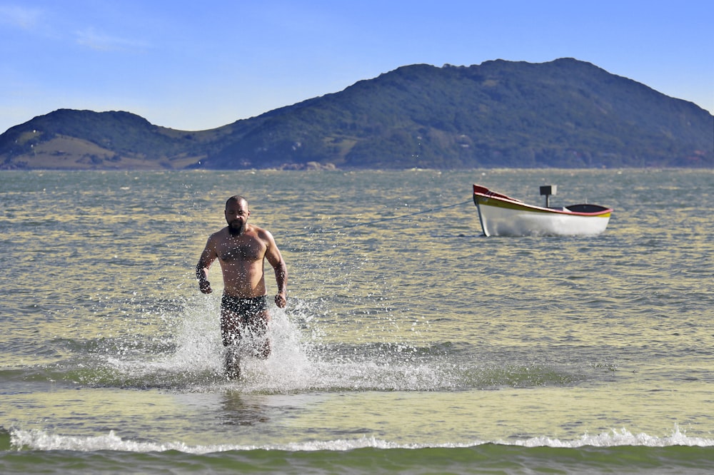 a man walking out of the ocean with a boat in the background