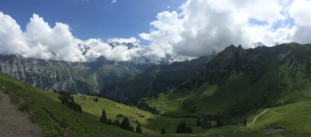 green grass field and mountains under blue sky and white clouds during daytime