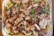 A tray filled with cooked shredded meat, likely chicken or pork, mixed with vermicelli noodles. The dish is garnished with chopped green onions, slices of lemon, and includes some vegetables such as carrots and cabbage. The meat appears to have a crispy texture.