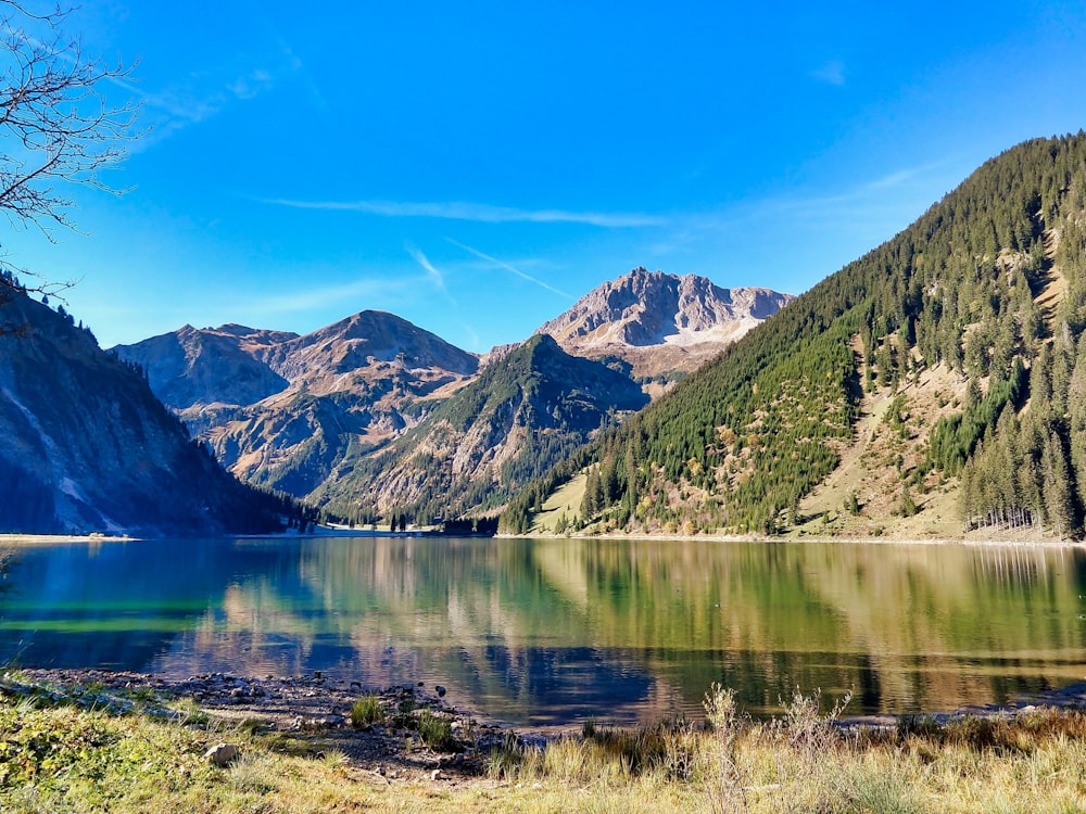 green and brown mountains beside lake under blue sky during daytime