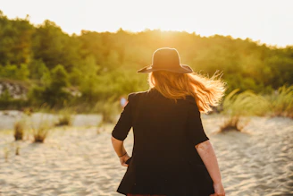 woman in black dress wearing brown fedora hat standing on river during daytime