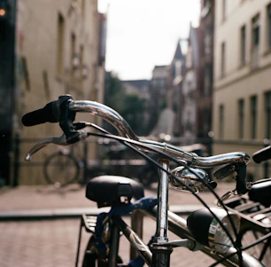 A close-up of a classic bicycle's polished chrome handlebars against a soft-focus urban backdrop.