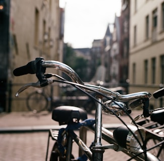 A close-up of a motorcycle handlebar with a blurred cityscape in the background.