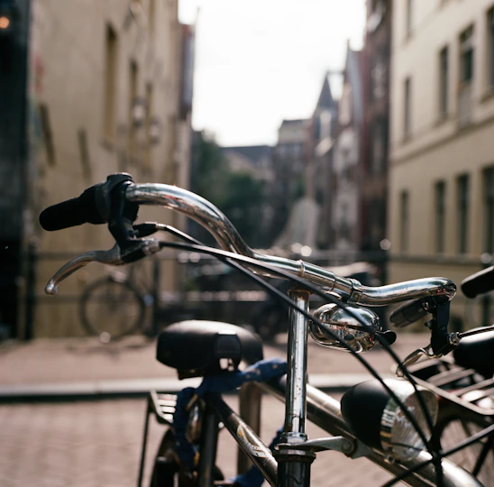 A close-up of a classic bicycle's polished chrome handlebars against a soft-focus urban backdrop.