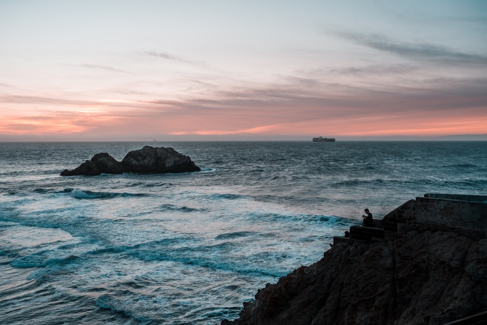 people standing on rock formation near sea during sunset