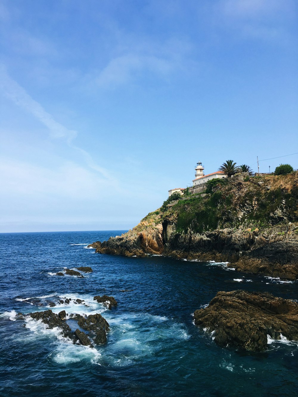 white lighthouse on green grass covered hill by the sea under blue and white cloudy sky