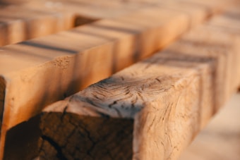 Close-up of a stack of unfinished wooden beams with visible wood grain and texture, captured under warm lighting.