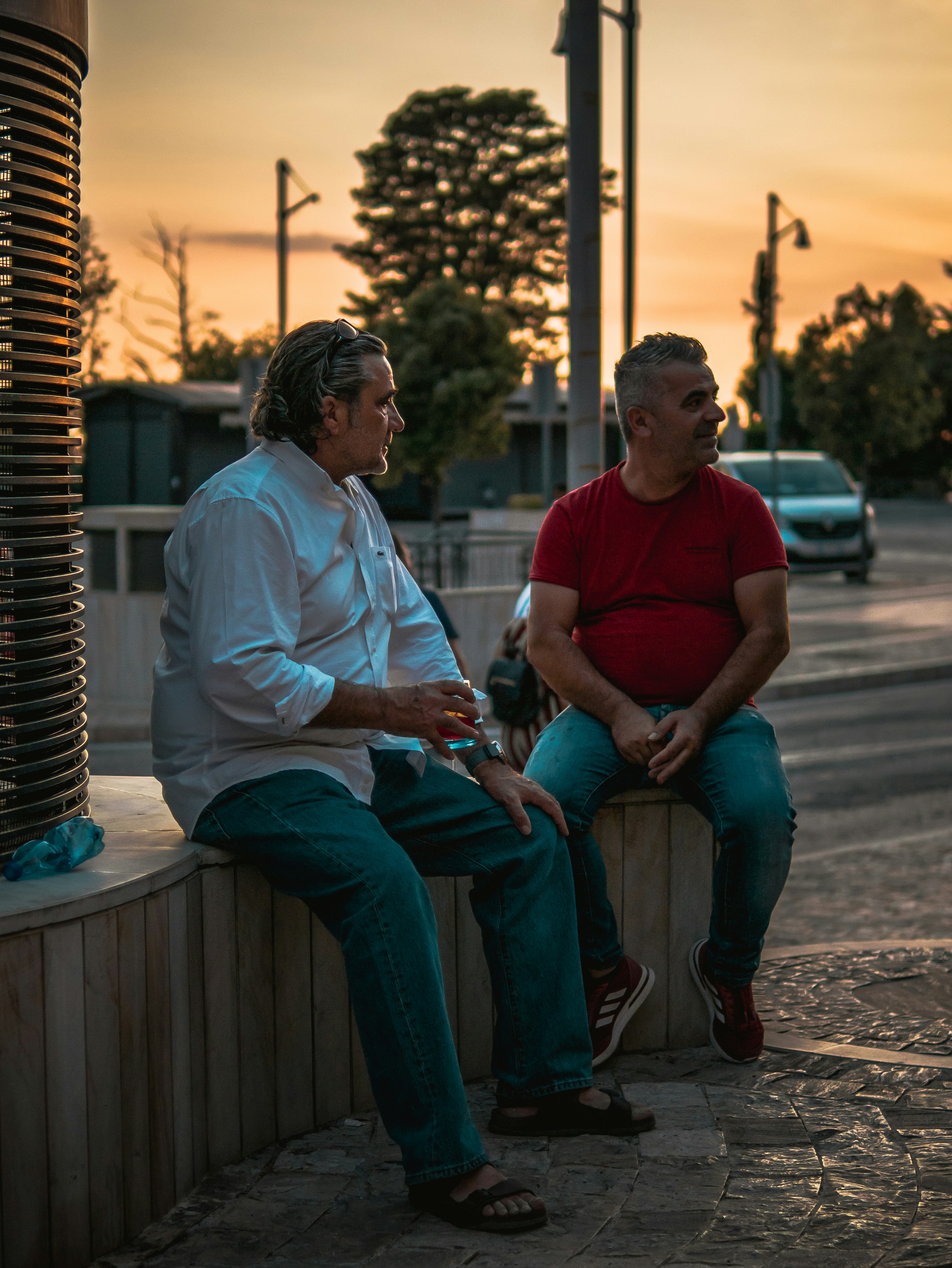 Two men sitting outside chatting and drinking during the sunset. Street photography.