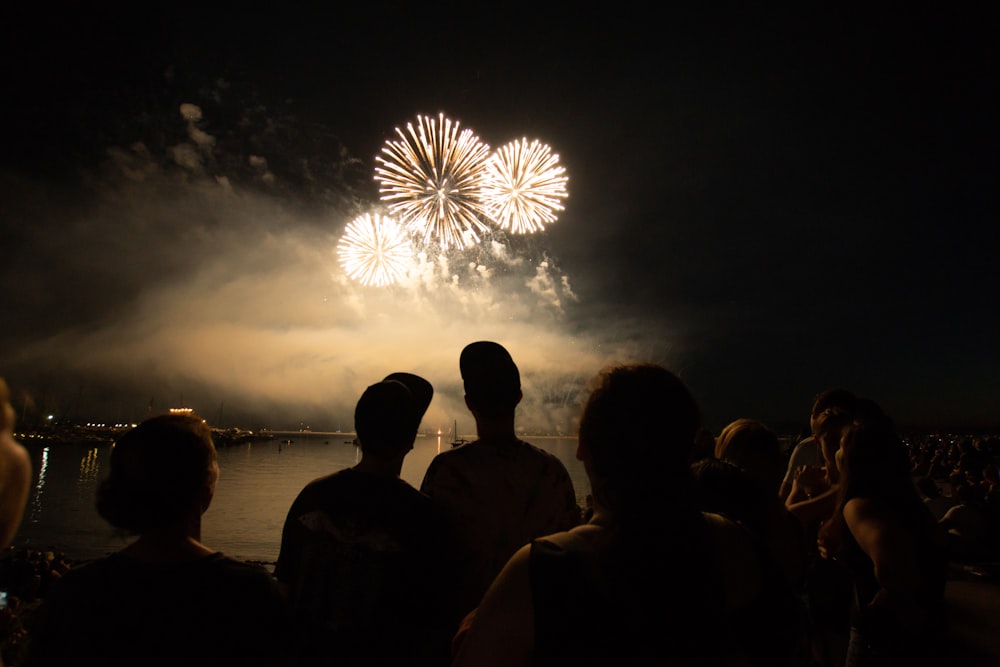 Silueta de personas que observan fuegos artificiales durante la noche