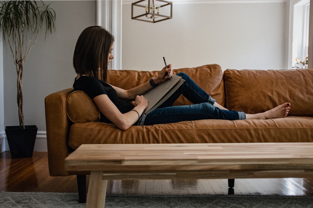 woman in black tank top and blue denim jeans sitting on brown sofa