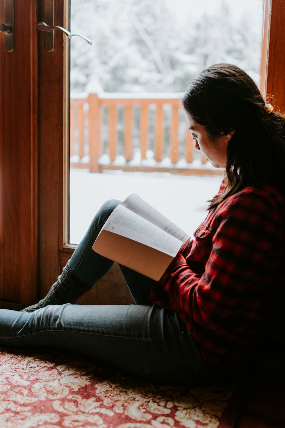 Femme en chemise à manches longues rayée rouge et noire et jean en denim bleu assise sur fond marron