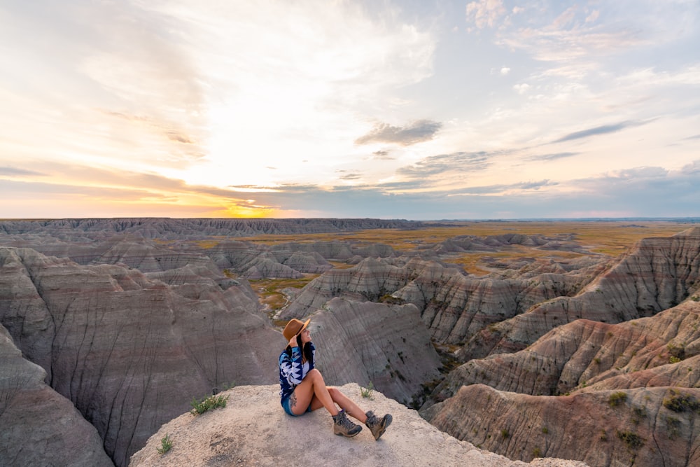 woman in blue tank top sitting on rock formation during daytime