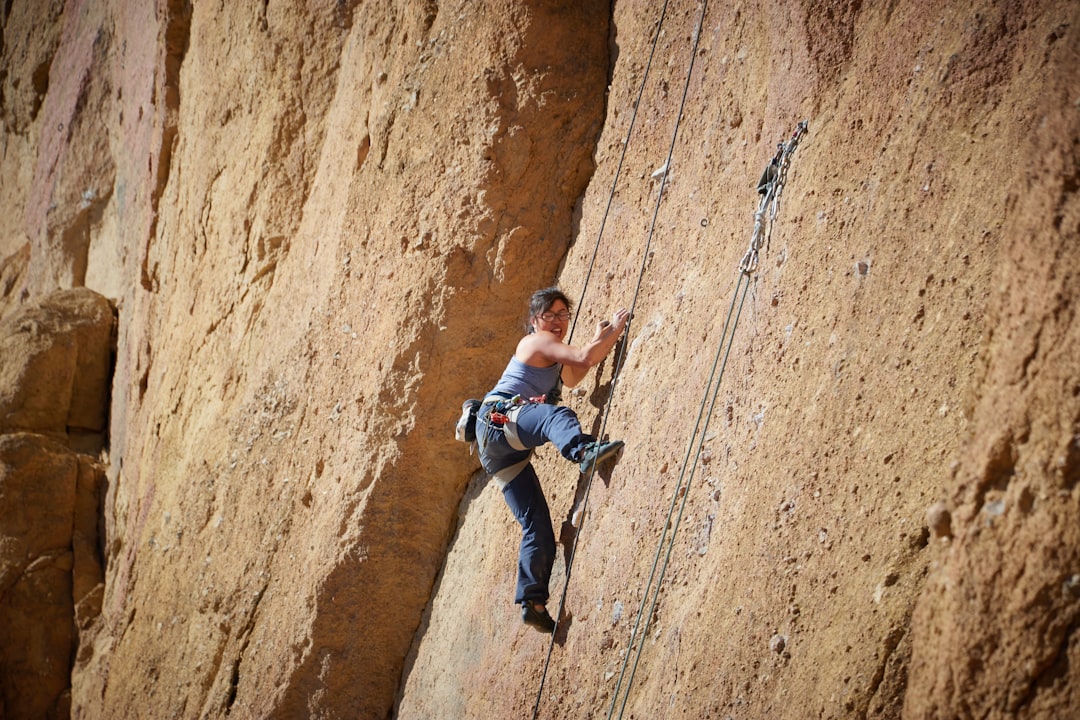 man in blue jacket climbing on brown rock, Climbing up Smith Rock in Bend Oregon
