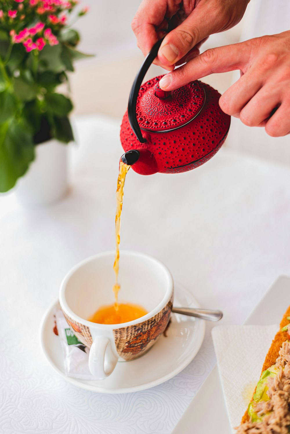 personne versant un liquide rouge sur une tasse à thé en céramique blanche