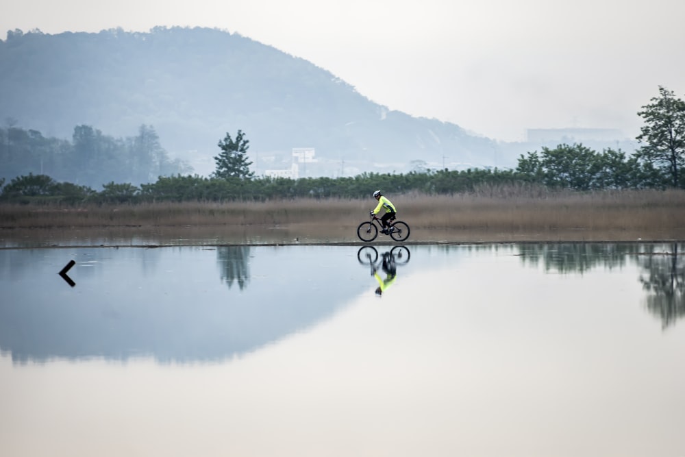 man in yellow jacket riding bicycle on lake during daytime
