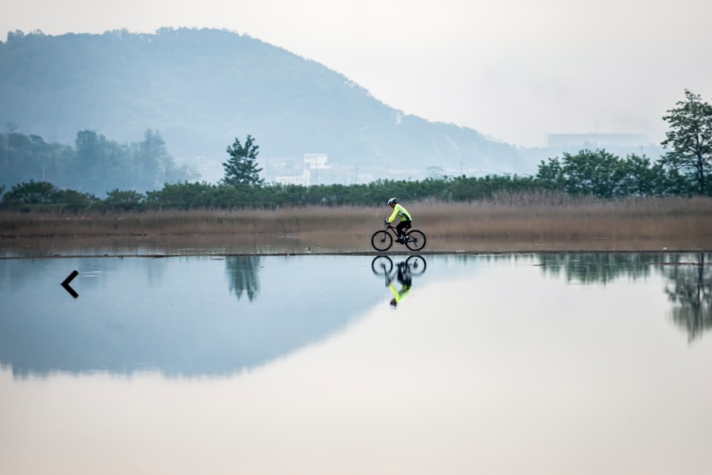 man in yellow jacket riding bicycle on lake during daytime