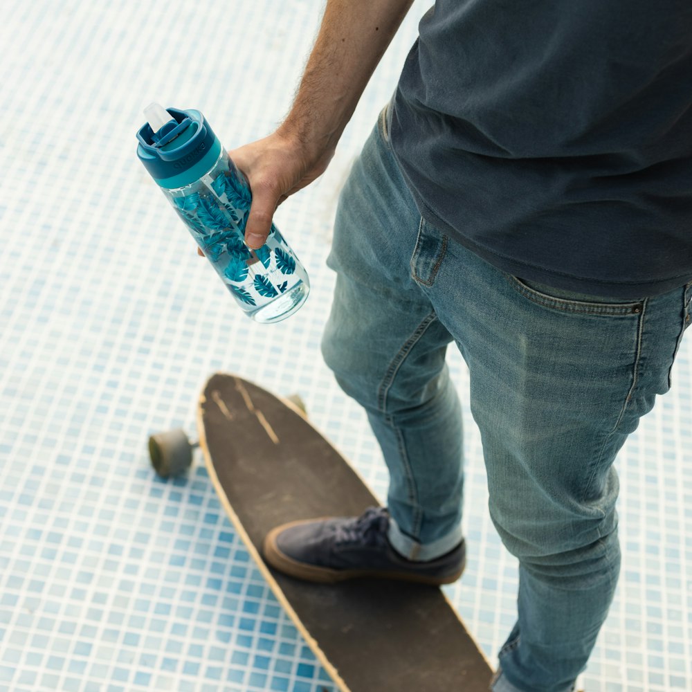 Mann in weißem Button-up-Hemd und blauer Jeans mit orange-weißer Flasche