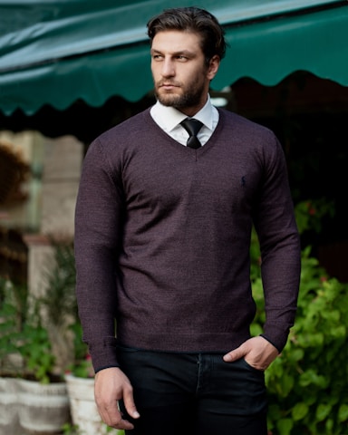 man in gray sweater standing near green trees during daytime