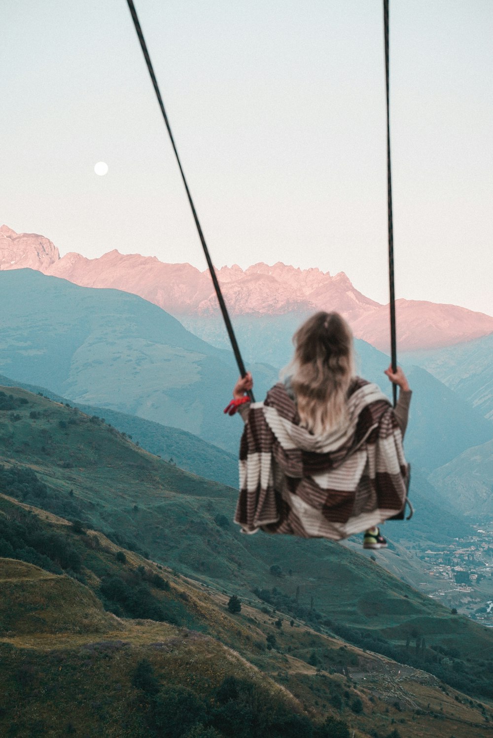 woman in black and white striped long sleeve shirt sitting on swing over the mountain during