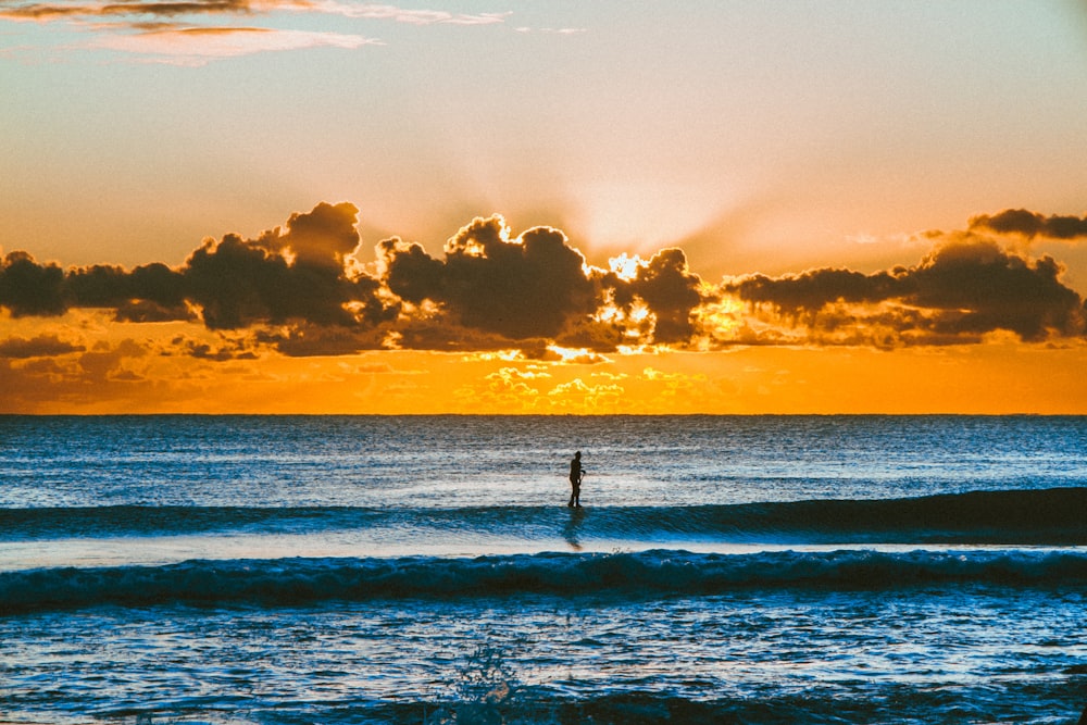 Persona de pie en la playa durante la puesta del sol