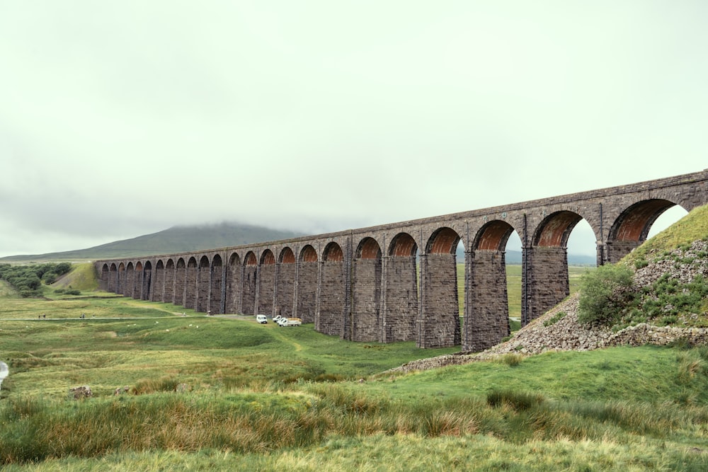 brown concrete bridge over green grass field under white sky during daytime