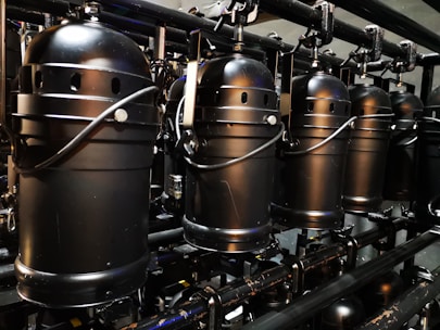 A row of industrial black stage lights is suspended from a metal framework. The lights feature cylindrical housings with handles and ventilation holes, suggesting they are meant for a theatrical or concert setting. The metallic surface and compact design indicate a robust construction.