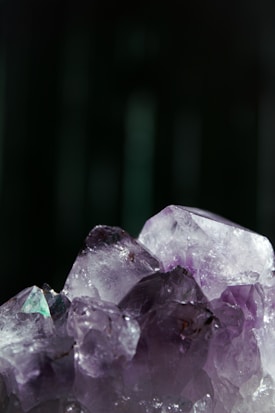An up-close view of a cluster of amethyst crystals with a rich purple hue, showcasing their natural, jagged edges and translucent quality set against a dark background.