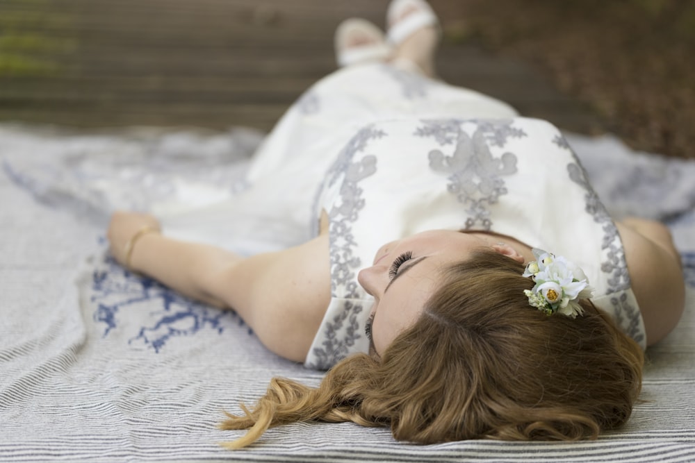 woman in white floral dress lying on white textile