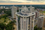 High-rise residential buildings with unique architectural designs feature prominently, surrounded by greenery and an urban landscape under a cloudy sky.