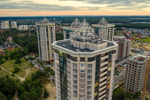 High-rise residential buildings with unique architectural designs feature prominently, surrounded by greenery and an urban landscape under a cloudy sky.