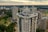 High-rise residential buildings with unique architectural designs feature prominently, surrounded by greenery and an urban landscape under a cloudy sky.