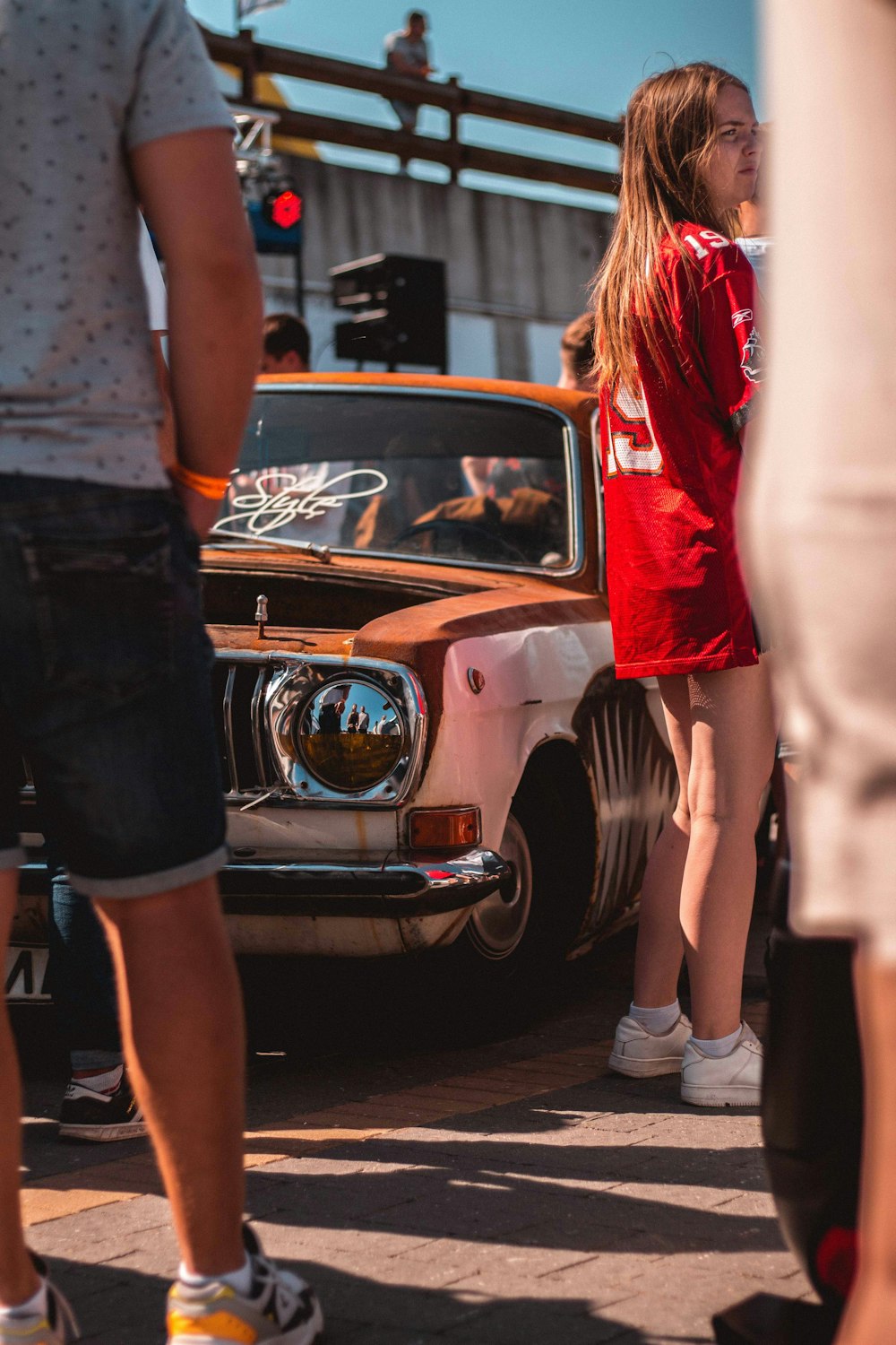 mulher na camisa vermelha que está ao lado do carro marrom e branco