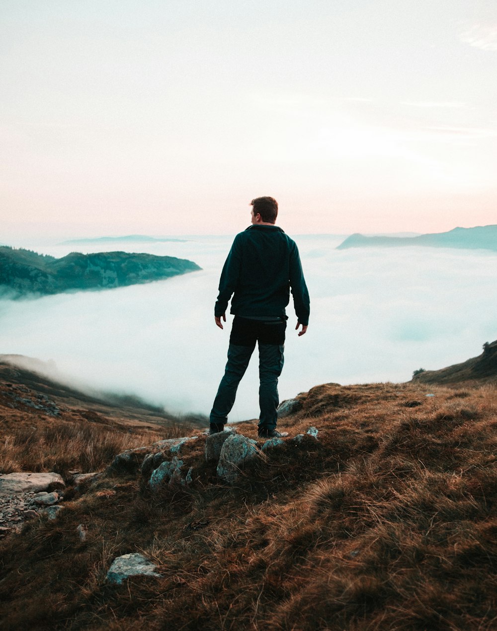 man in black jacket standing on brown rock near body of water during daytime