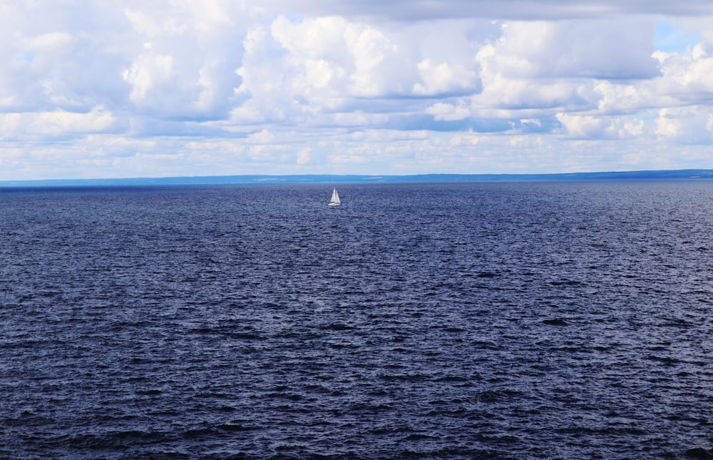 white sailboat on sea under white clouds and blue sky during daytime